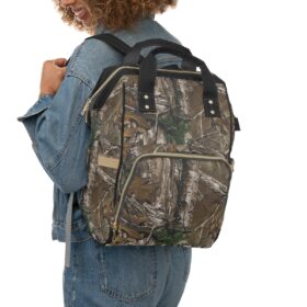 A person with curly hair in denim, smiling, carries the Camo Diaper Backpack With Hunting Concealment Camouflage Realtree Xtra over one shoulder.
